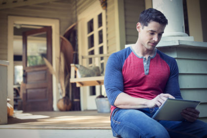 A man sitting relaxing in a quiet corner of a porch using a digital tablet scaled