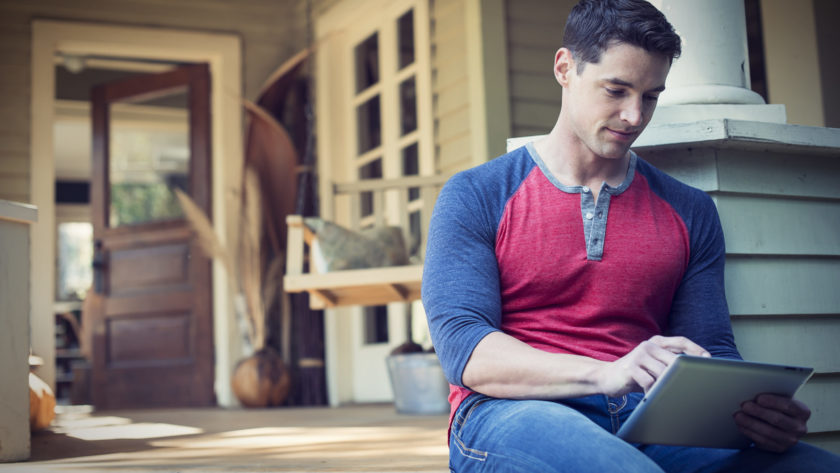 A man sitting relaxing in a quiet corner of a porch using a digital tablet scaled