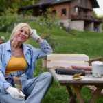 Happy senior woman sitting and resting while doing paint craft outdoors in garden