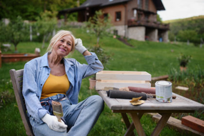 Happy senior woman sitting and resting while doing paint craft outdoors in garden