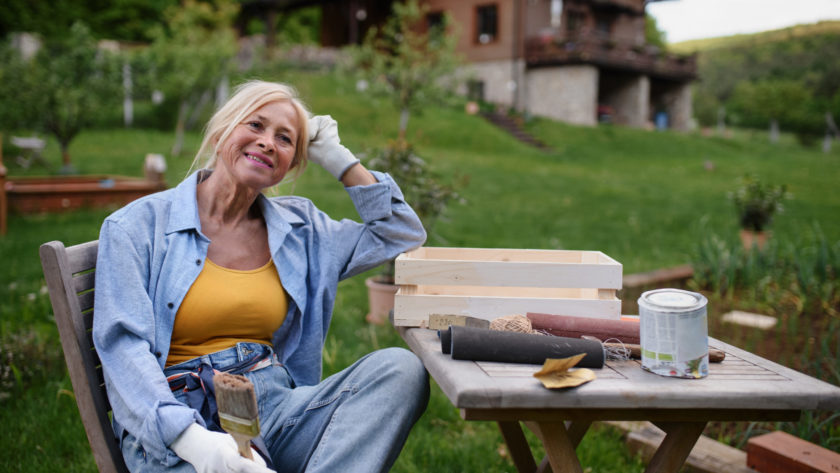 Happy senior woman sitting and resting while doing paint craft outdoors in garden