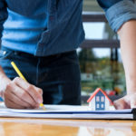 Architect holding a yellow pencil drawing house.