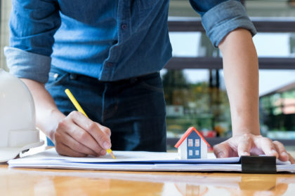 Architect holding a yellow pencil drawing house.