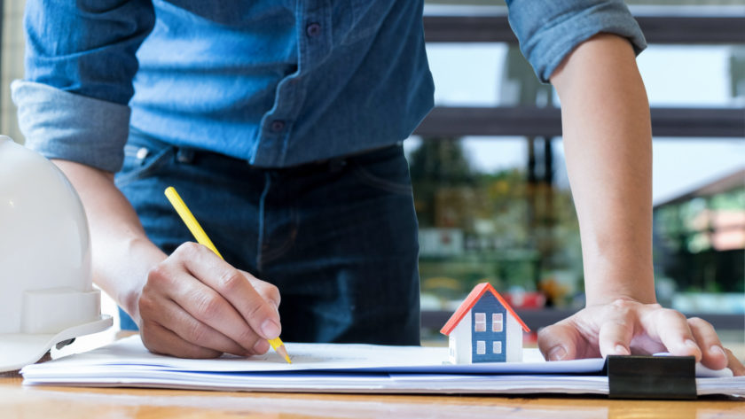 Architect holding a yellow pencil drawing house.