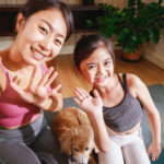 Asian woman yoga teacher and little girl filming yoga online class on video.