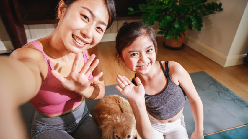 Asian woman yoga teacher and little girl filming yoga online class on video.